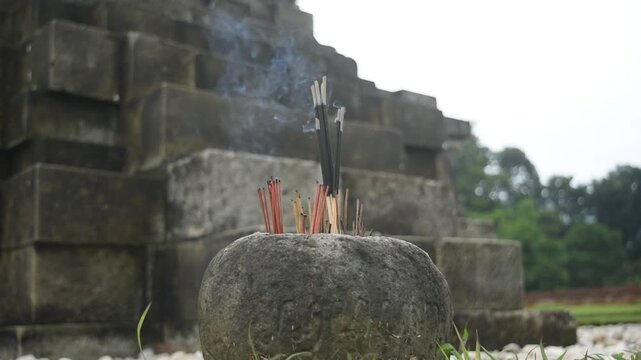Close-up of incense glowing in a stone holder beside a temple