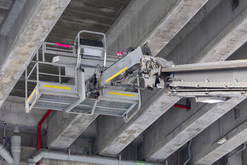 Naklejka premium A grey crane with a bucket on top of it is in the air. Mobile construction crane for rent and sale. Aerial work platforms of a cherry pickers under the bridge. Boom lifting machine.
