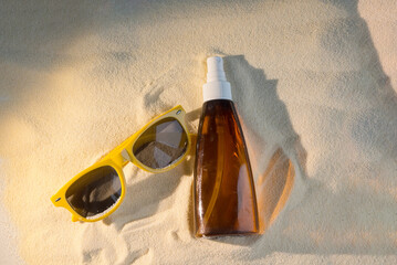 Sunglasses and sunscreen bottle on sandy beach. The sunglasses are yellow, and the sunscreen is in a brown bottle. Ideal for summer and vacation themes. © Татьяна Зернова