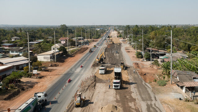 Aerial view of road construction with heavy machinery and trucks upgrading highway infrastructure in rural area, symbolizing development and economic growth.