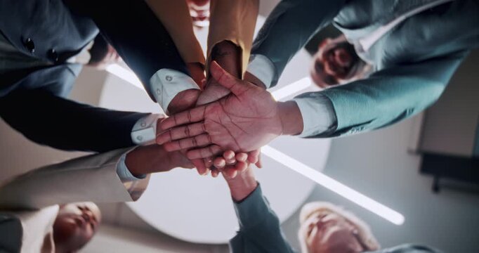 Below, teamwork and business people in office with hands together, solidarity or motivation for goals. Happy, colleagues and huddle in workplace with connection, collaboration or synergy for success.