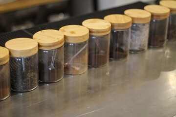 Row Of Glass Spice Jars With Wooden Lids On Stainless Counter In Kitchen Cafe