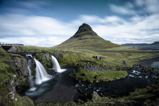 View of cascading waterfalls plunge into the river beneath the majestic Kirkjufell mountain under a starlit sky, Grundarfjardarbaer, Grundarfjardarbaer, Iceland.