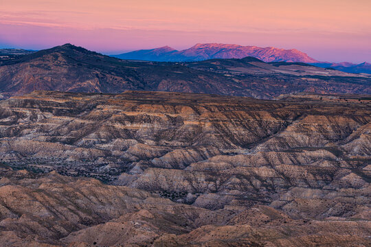 View of eroded badlands sculpted by time under a pastel sky, where rugged terrain meets distant mountains, Gorafe, Andalucia, Spain.