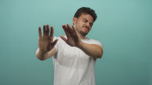 Young hispanic man palms out stop gesture, bare hands and face visible, studio teal backdrop; repulsion refusal avoidance.