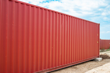 Fototapeta premium Side view of a long red corrugated shipping container on an outdoor storage site. international logistics, industrial transport, cargo storage.