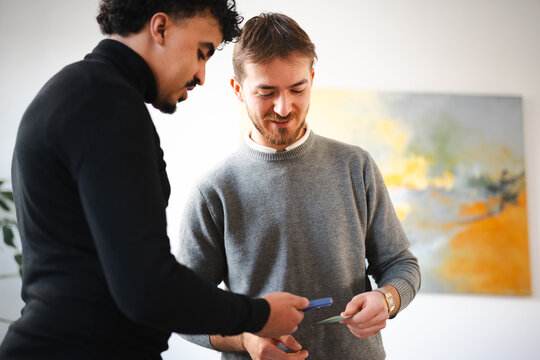 Two men are looking at a card and a mobile device, possibly discussing a transaction or sharing information.