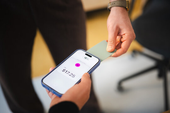 A person holds a smartphone displaying a payment of $17.25, while another person presents a card for contactless payment.