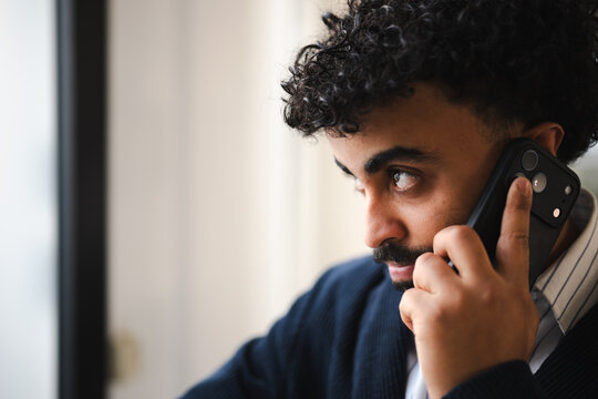 A man with curly hair talks on his mobile phone, his gaze directed away from the camera, suggesting deep thought or concentration during a business call.