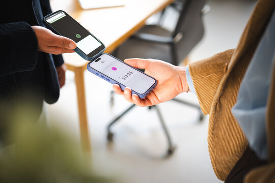 Two people are making a contactless payment by holding their mobile phones together, one displaying a payment amount of $17.25.