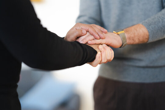 Two people hold hands, showing support and connection. One person wears a black shirt, the other a grey sweater and a watch.