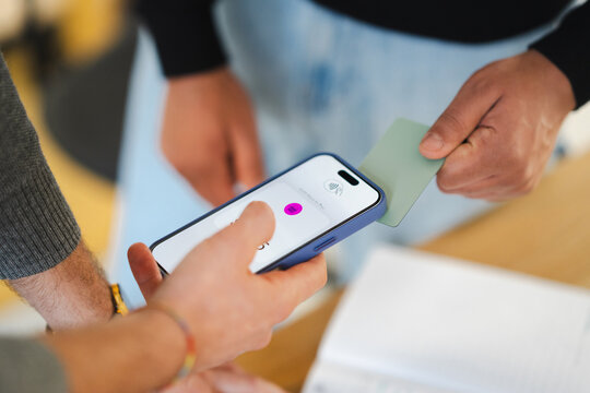 A person holds a smartphone with a payment app open, while another person presents a card for contactless payment.