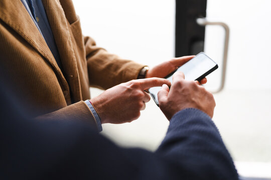 Two men in business attire are looking at a smartphone together, one pointing at the screen.