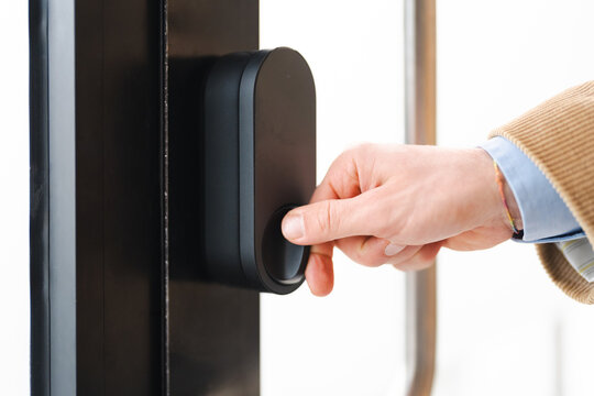 A person's hand turns a knob on a modern smart lock. This action signifies entry or exit, highlighting convenience and security in a home or office setting.