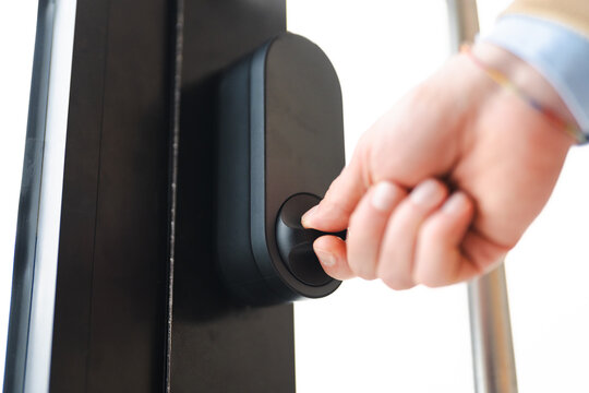 A person's hand turns a knob on a modern door lock. This action signifies entry or exit, security, and smart home technology.