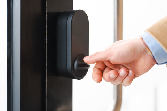 A person's hand presses a button on a modern smart lock on a door, indicating access and security.