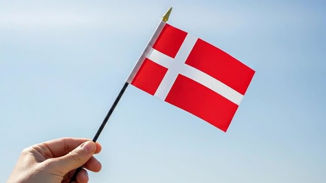 Hand Holding the National Flag of Denmark Against a Clear Blue Sky