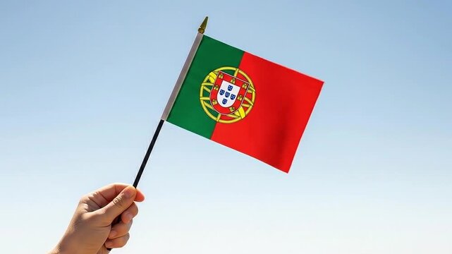 Hand Holding Portuguese National Flag Waving Against Clear Blue Sky