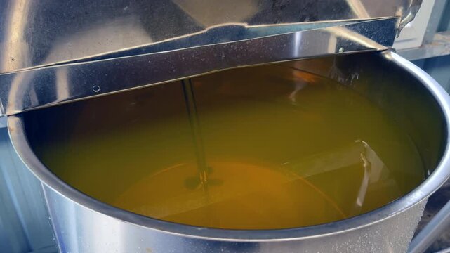 A professional stainless steel mixing vat containing golden liquid or essential oil. Perfect for industrial production of cosmetics, shampoos, or chemical ingredients in a factory setting.