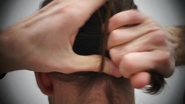 Close-up of the back of a man's head pulling his hair back into a ponytail