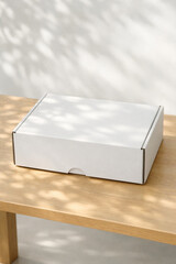 Blank corrugated cardboard mailer box mockup on a wooden table with dappled sunlight and leaf shadows.
