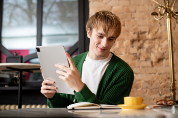 Obraz premium Young man enjoys a relaxing moment in a modern cafe with his tablet and coffee
