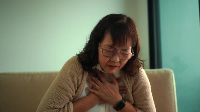 Unhealthy elderly woman having chest pain and difficulty breathing alone at home, heart attack symptoms and cardiac emergency in retirement age, urgent medical care needs and health life insurance.
