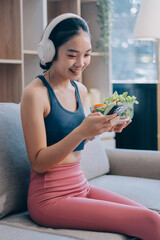 Fit young Asian women in activewear sitting on yoga mat and eating fresh vegetable salad after workout, representing clean eating, fitness lifestyle, wellness routine and health balance.