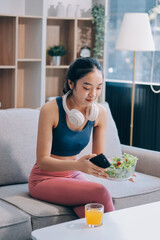 Fit young Asian women in activewear sitting on yoga mat and eating fresh vegetable salad after workout, representing clean eating, fitness lifestyle, wellness routine and health balance.