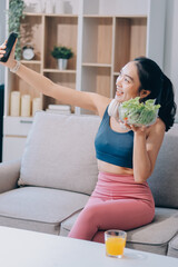 Fit young Asian women in activewear sitting on yoga mat and eating fresh vegetable salad after workout, representing clean eating, fitness lifestyle, wellness routine and health balance.