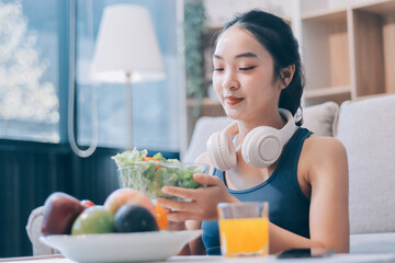 Fit young Asian women in activewear sitting on yoga mat and eating fresh vegetable salad after workout, representing clean eating, fitness lifestyle, wellness routine and health balance.