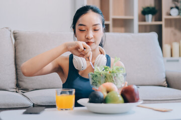 Fit young Asian women in activewear sitting on yoga mat and eating fresh vegetable salad after workout, representing clean eating, fitness lifestyle, wellness routine and health balance.