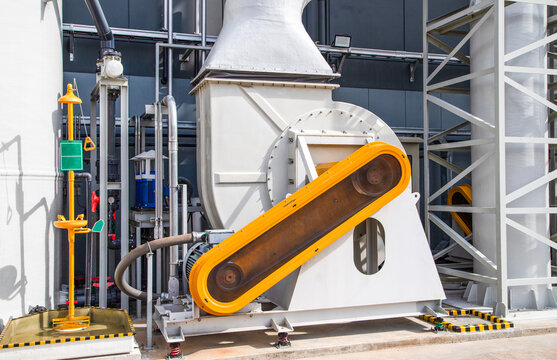 Industrial centrifugal fan blower with motor and orange belt guard in a modern factory.Close up of industrial air blower equipment with safety belt drive guard.