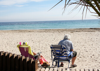 Playa, cielo azul y matrimonio turista con tumbonas en la arena tomando el sol de viaje en vacaciones de verano 