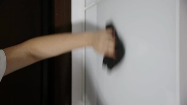 Human hand wiping white wall surface with dark cloth. Cleaning action. Removing dust or stains. Home interior. Concept of domestic work, house maintenance and cleanliness.
