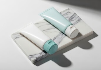 Two cosmetic tubes on a marble slab with shadows on white surface