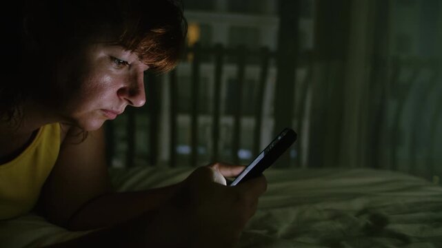 Female Relaxing on Bed in Evening Scrolling Through Messages and Online Content on Mobile Phone
