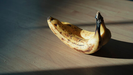木目のテーブルに置かれたバナナ 差し込む自然光とドラマチックな影 静物 / Ripe bananas on wooden table with dramatic natural light and long shadows, still life