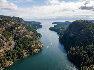Fototapeta premium Aerial view of a wide, calm river flowing between lush green forested hills and mountains towards the ocean under a cloudy sky.