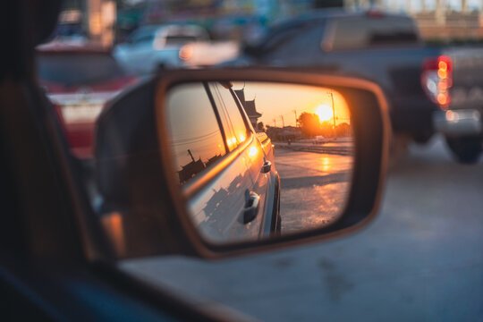 Sunset reflection in a car side mirror on a city street in Thailand,A cinematic shot showing a vibrant golden sunset reflected in a car's rearview mirror. The reflection captures the sun low.