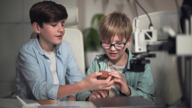 Two school boys are actively discussing the parts just printed on the 3D printer