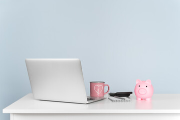 Laptop and piggy bank on white desk against blue wall