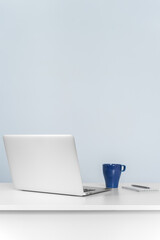Laptop and coffee mug on white desk against blue wall