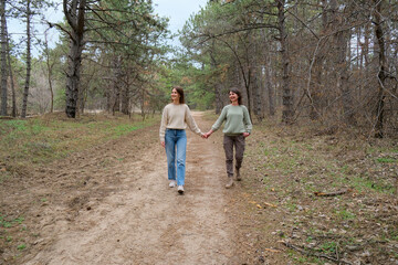 Obraz premium Mother and daughter are walking hand in hand along a dirt path in a natural park, enjoying their connection, family bond, and togetherness surrounded by trees and dry grass