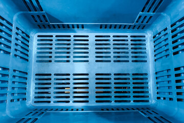 Overhead perspective of an empty blue plastic storage crate with perforated bottom and sides
