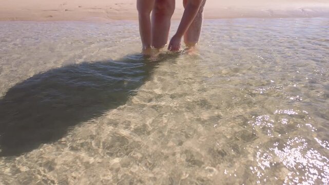 A woman washes her feet in the sea after walking barefoot on a tropical summer beach