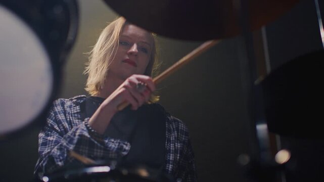 Woman drummer plays a drum kit, drumstick. Female musician beats a rock rhythm on drums, cymbals. Girl artist is rehearsing in a room or performing on festival stage. Alternative indie band in club