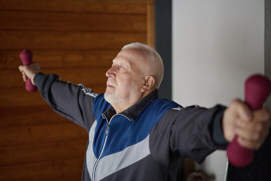 Elderly man exercises with dumbbells in a room during daylight hours for strength training and fitness
