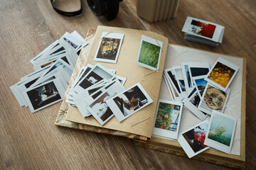 Collection of printed photos scattered across a table next to a photo album and camera during afternoon light © mira_y