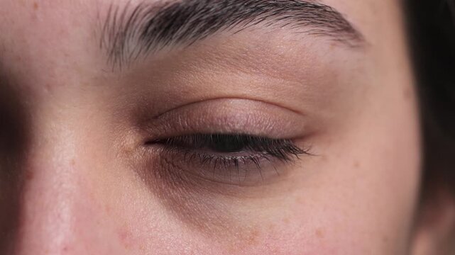 4K video macro closeup of young woman opening eye, subtle smile visible in her eye and closing it, no makeup and natural expression, studio shot on white background